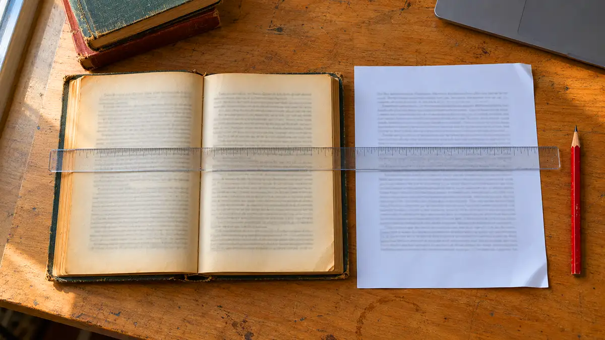 Отворена стара книга и разпечатка на превода, подравнени с прозрачна линия на един и същ ред